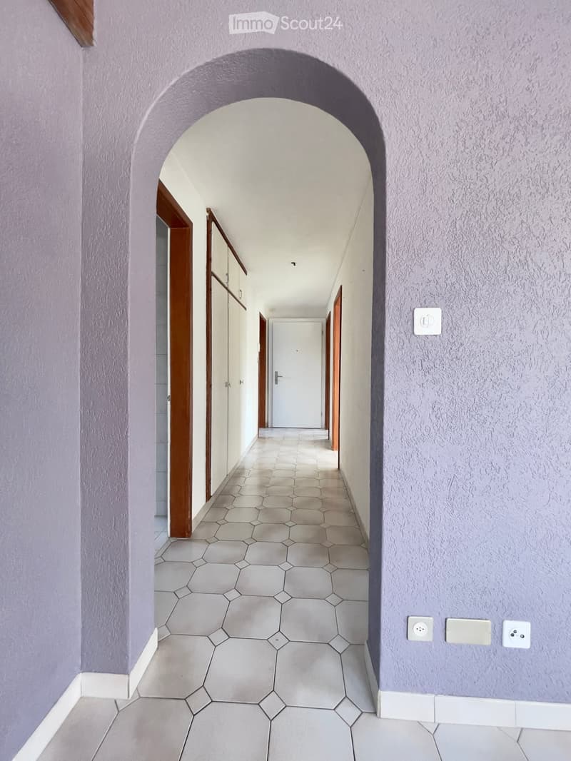 empty hallway with arched entry, white hexagonal tiles, wooden doors, white walls, electrical outlets