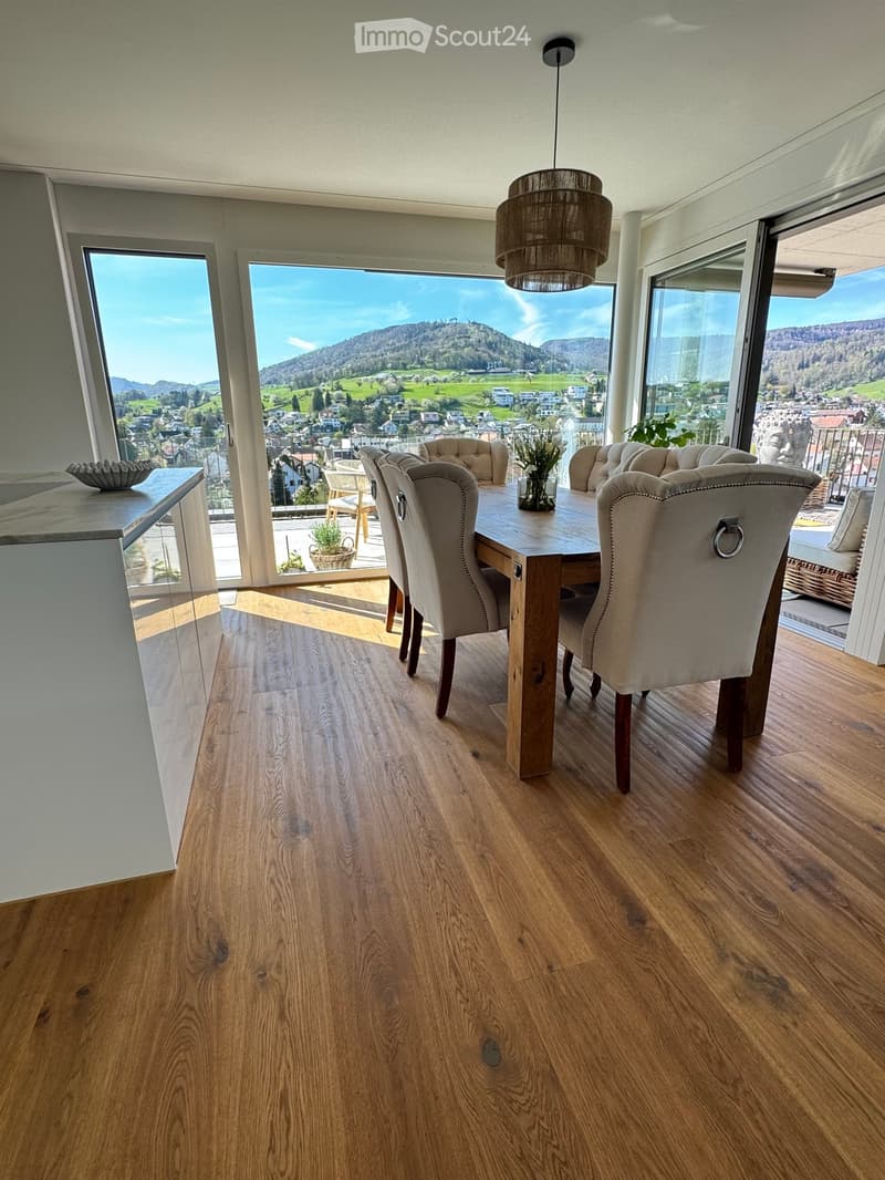 Dining room with wooden floor, large windows, dining table, chairs, and a view of the mountains