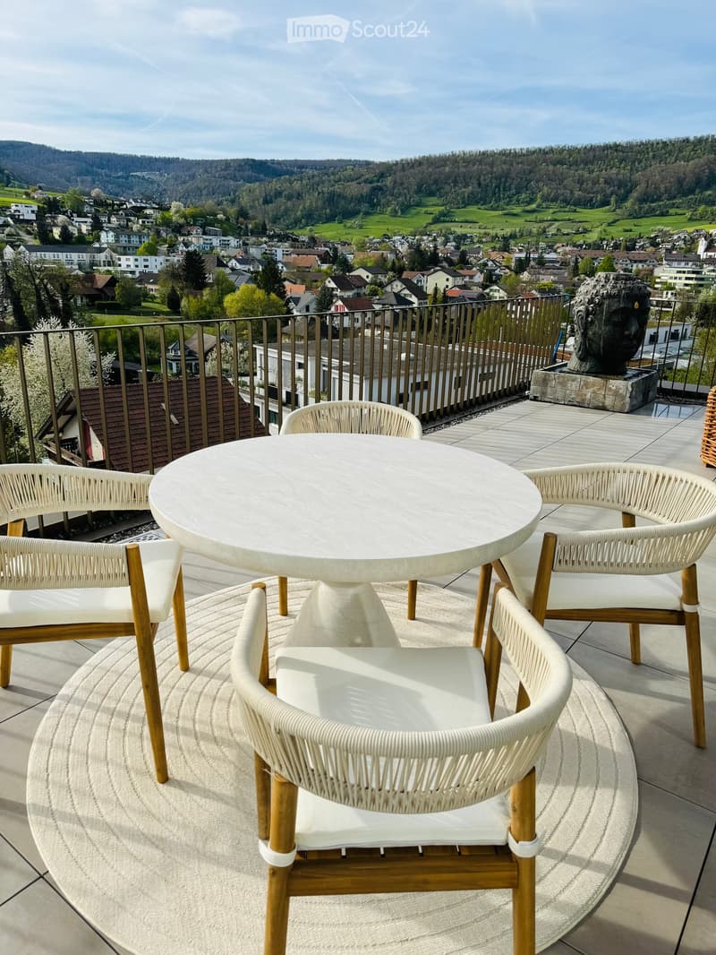 Balcony area with a circular marble table, four wicker chairs, circular rug, balcony railing, scenic mountain view in the background