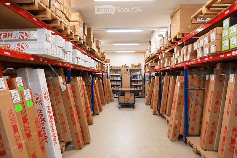 Warehouse with high ceilings, metal shelving units filled with cardboard boxes, and a small cart in the center.
