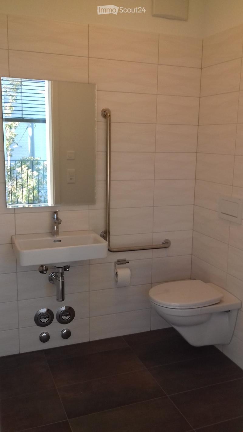 Modern bathroom with white tiles, a sink, toilet, mirror, and a handrail for accessibility.