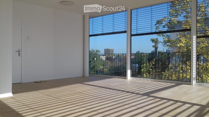 Empty room with large windows, wooden floor, and a door. No furniture or equipment present.