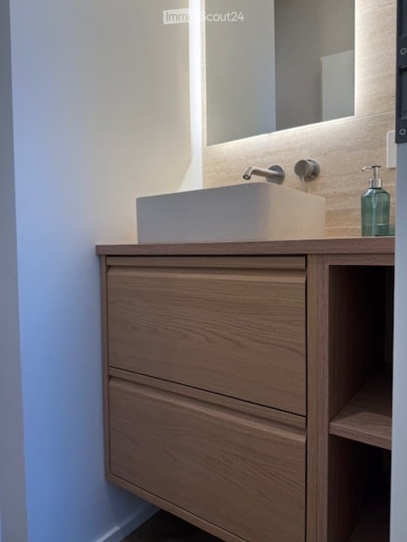 Modern bathroom with a sleek wooden vanity, integrated sink, and a large mirror with LED lighting above.