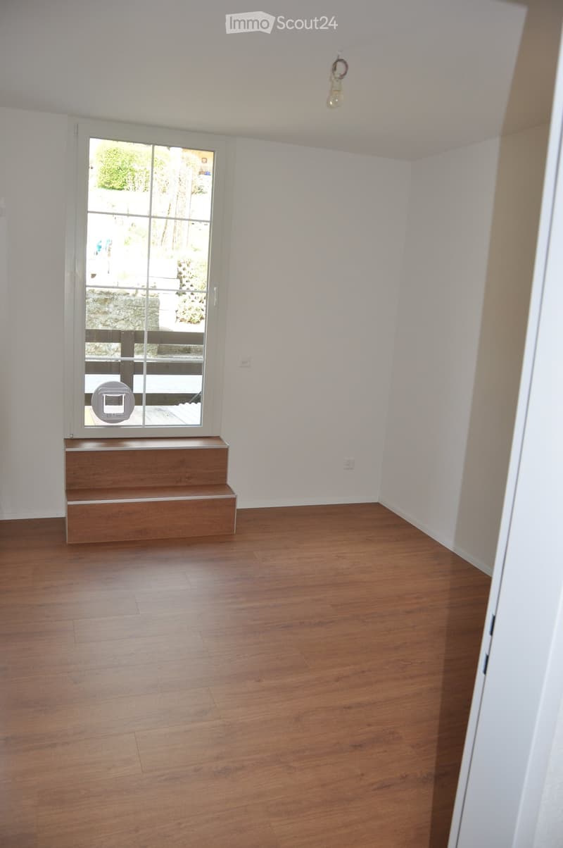 Empty room with wooden flooring, white walls, and a window with a small wooden bench beneath it.