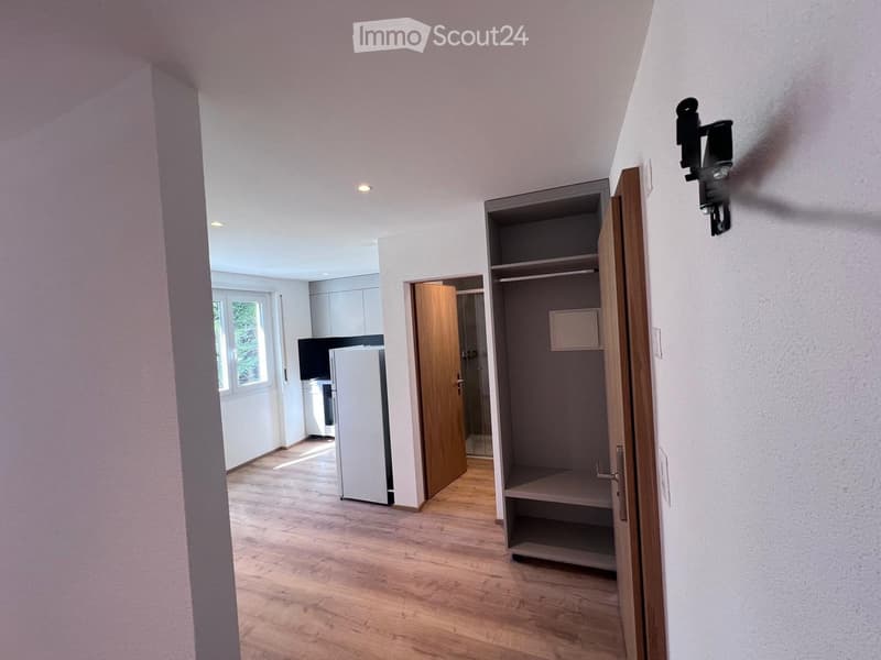 wooden floor, white walls, open door leading to other room, wooden wardrobe, open door to kitchen, white refrigerator, glass window