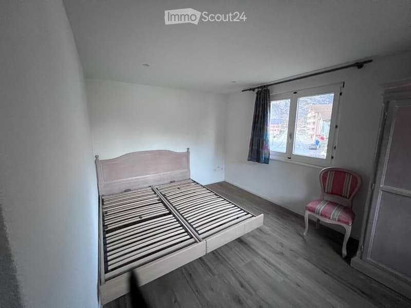 wooden bed with slats, striped chair, power outlet, large window with curtains, wooden floor