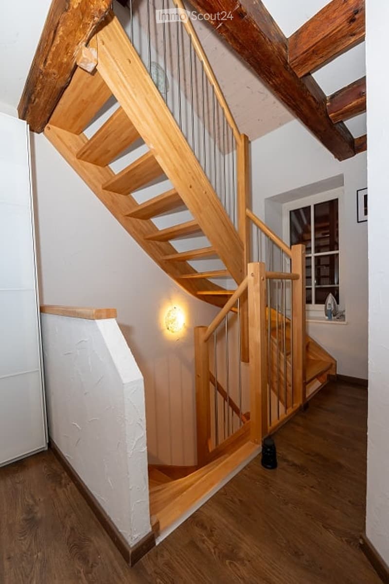 Wooden staircase with metal railing, warm lighting, and exposed wooden beams on the ceiling.