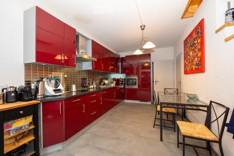 Modern kitchen with red cabinets, stainless steel appliances, and a dining area with a glass table and chairs.