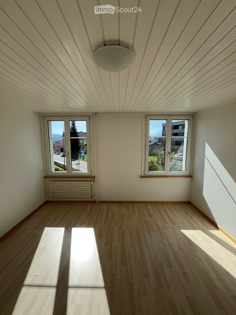 Empty room with wooden flooring, white walls, large windows, and a ceiling light fixture. No furniture or equipment present.