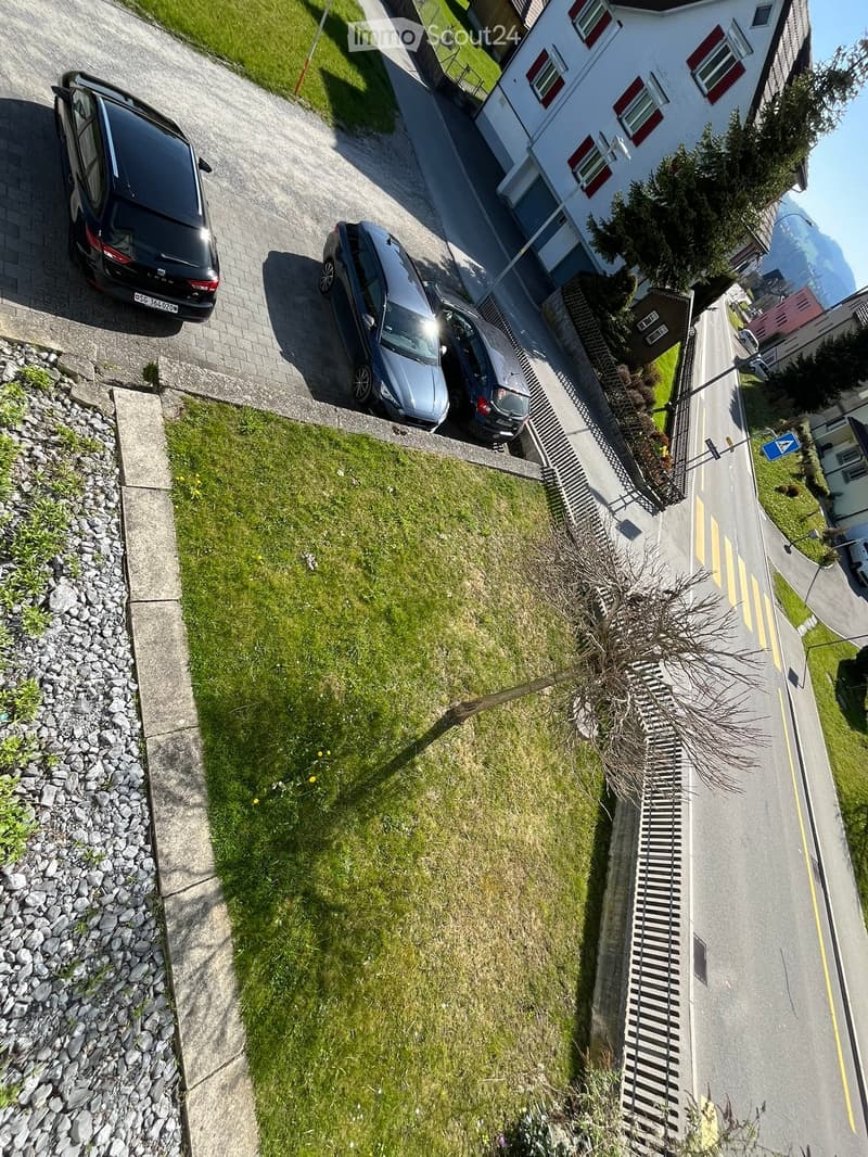 Aerial view of a two-story house with a driveway, three parked cars, and a small garden area.