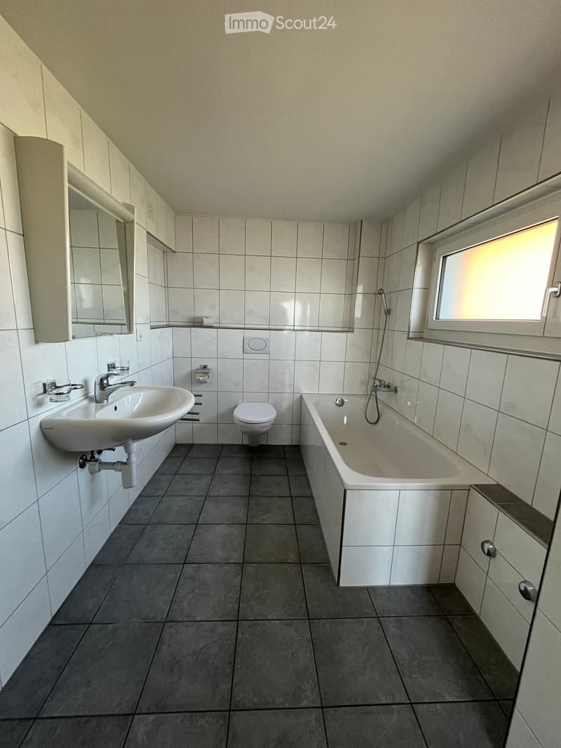 Modern bathroom with white tiles, a sink, toilet, bathtub, and a mirrored cabinet.
