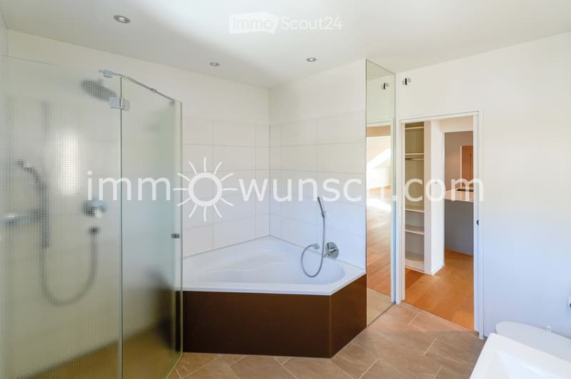 Modern bathroom with a bathtub, glass-enclosed shower, and a visible faucet. The space features tiled walls and a wooden floor.