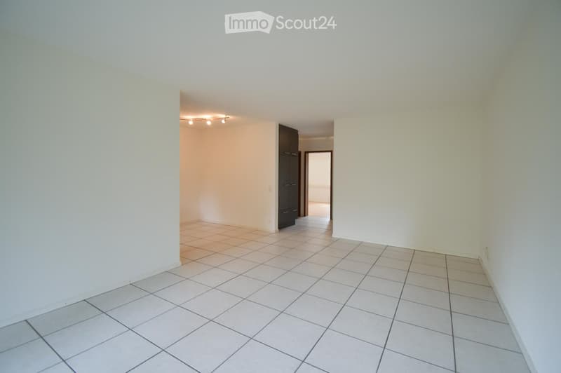 Empty room with white tiled flooring and white walls, featuring a doorway leading to another room with a dark cabinet.