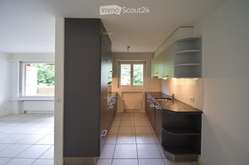 Modern kitchen with dark cabinets, light countertops, and a sink. The space features tiled flooring and large windows providing natural light.