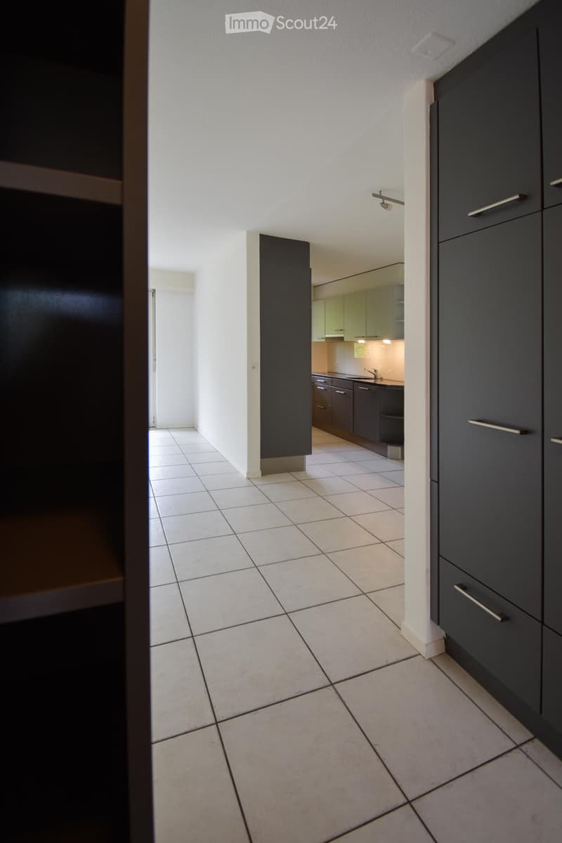 A clean, modern hallway with tiled flooring and white walls, leading to a kitchen area with dark cabinets and a sink.