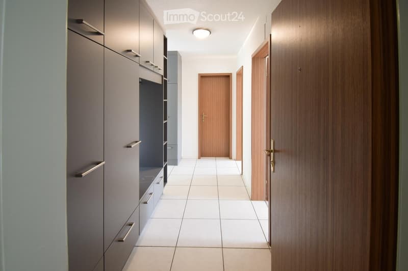 Modern hallway with white tiled flooring, grey cabinetry on one side, and wooden doors leading to other rooms.