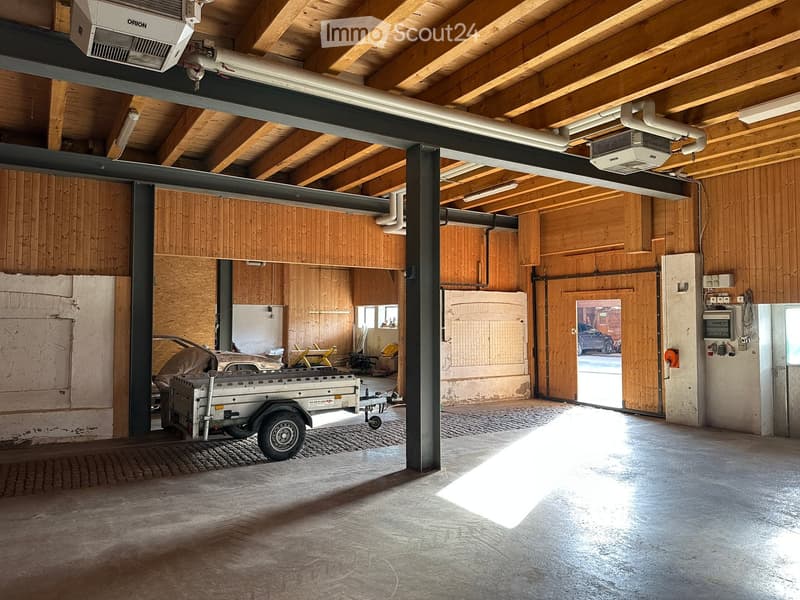an empty storage area with exposed wooden beams, open door, air conditioning units, piped heating and ventilation systems, a trailer parked, a car parked outside, brick floor