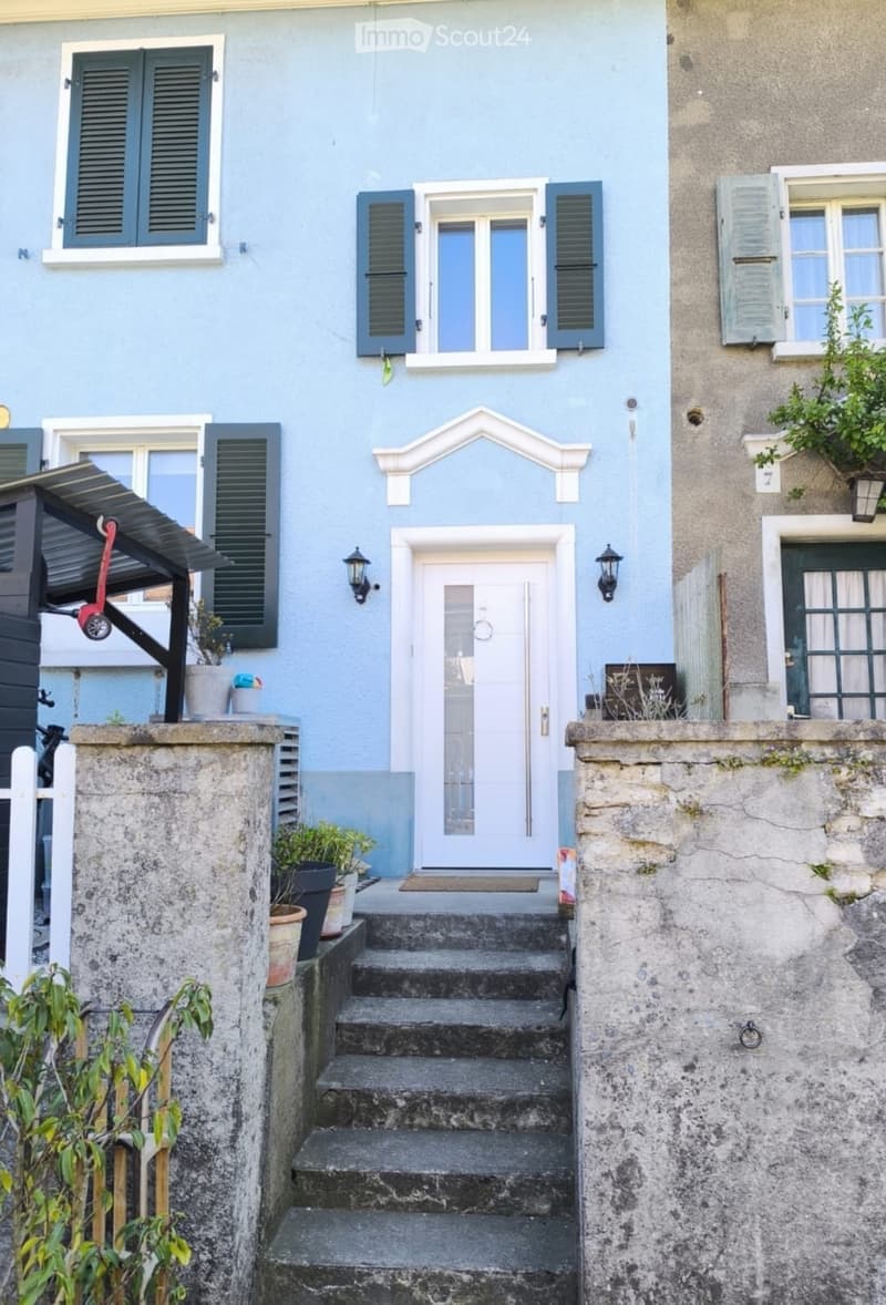 Two-story house with light blue exterior, white trim, multiple windows with shutters, and a central entrance with steps leading up to it.