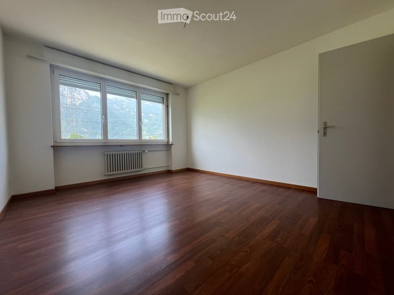 Spacious bedroom with large windows, hardwood flooring, and a radiator on the wall.