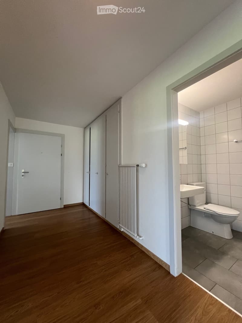 {"visible_features":[],"type":"Room","description":"The image shows a bedroom or living space with a wooden floor, white walls, and a bathroom visible through an open doorway. The room has a closet or wardrobe along one wall and a radiator. The bathroom a