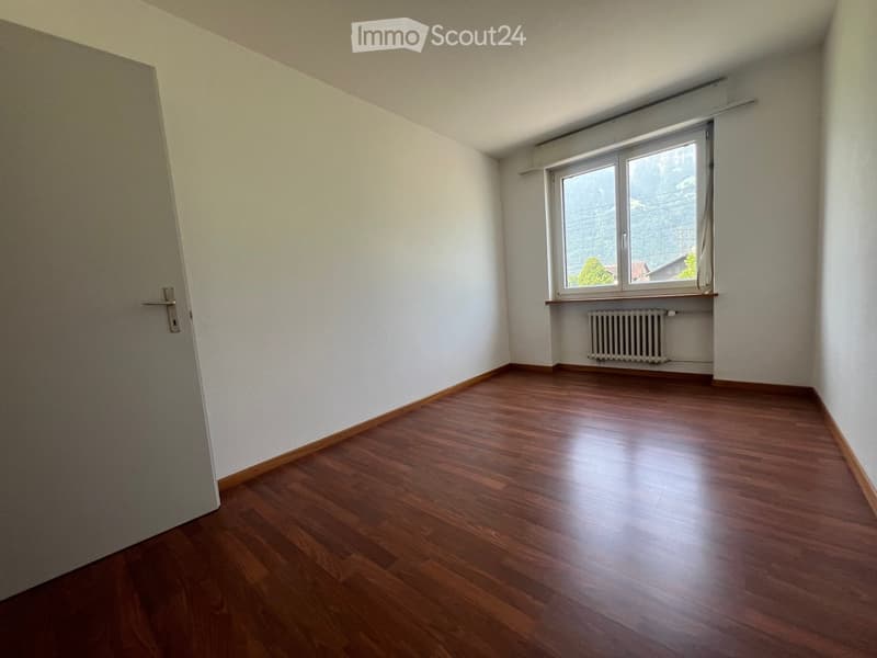 Spacious bedroom with hardwood flooring, white walls, and a large window providing natural light. The room appears to be empty, ready for furnishing and personalization.