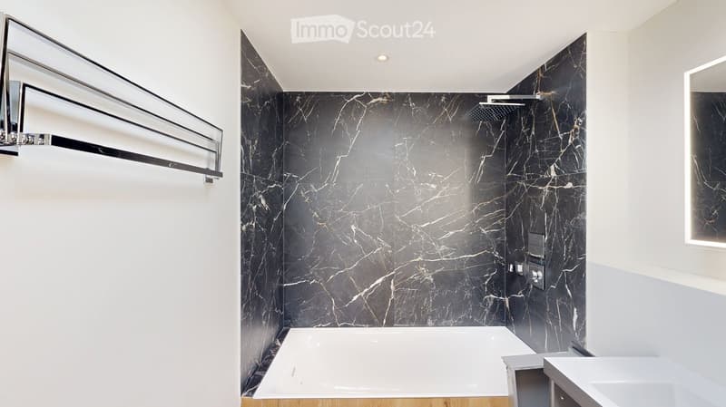 Modern bathroom with a large bathtub, marble walls, a showerhead, and a sleek mirror above the tub.