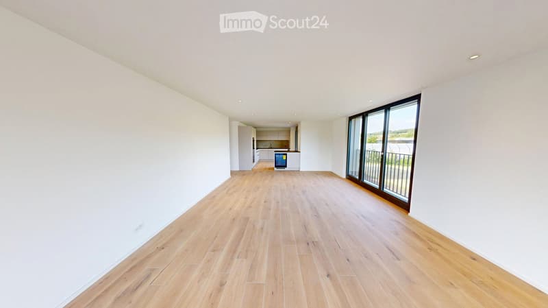 Empty room with light wooden flooring, white walls, and large windows leading to a balcony. The room is unfurnished and has a modern, minimalist design.