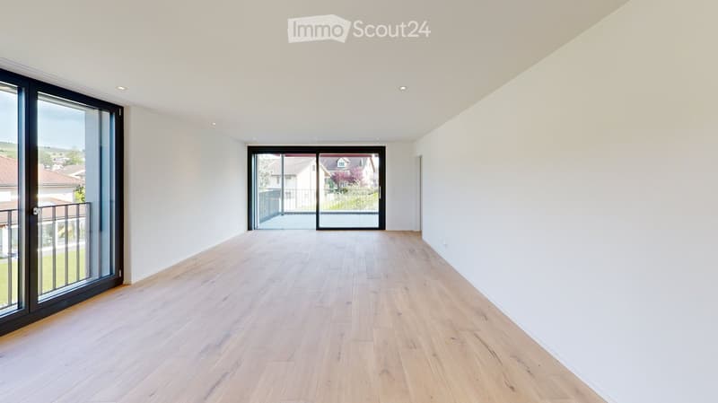 Empty room with light wooden flooring, white walls, and large sliding glass doors leading to a balcony and outdoor area.