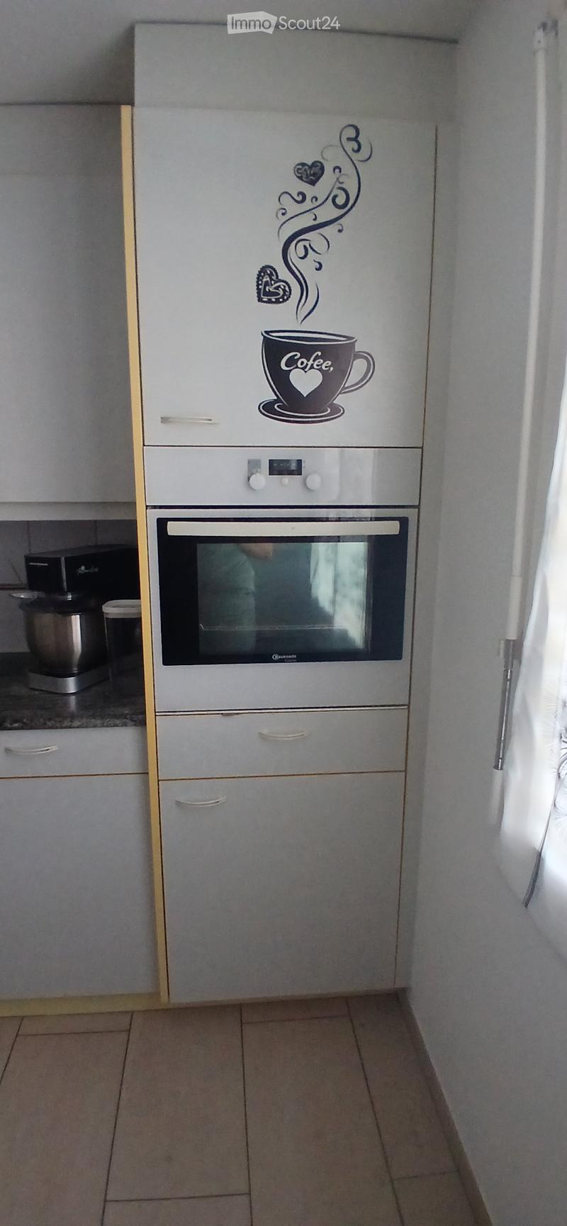 Modern kitchen with white cabinets, a built-in oven, and a decorative sticker featuring a coffee cup and swirls on the cabinet door.