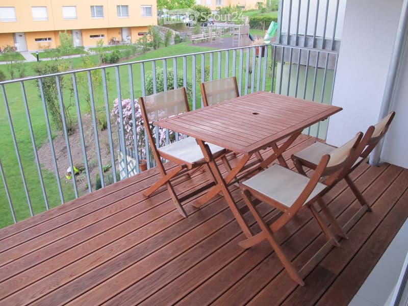 Balcony with wooden decking, metal railing, and a small wooden table with four folding chairs.