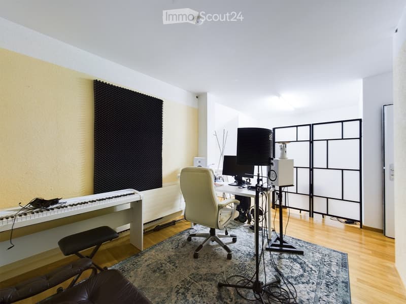 A well-furnished room with a piano, a desk with a computer and screen, a chair, a lamp, a screen divider, and a leather chair.