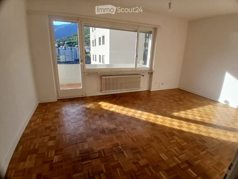 Empty room with wooden flooring, large windows, and a radiator. No furniture or equipment present.