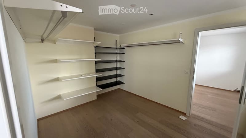 Empty closet with white and black shelving units, wooden flooring, and white walls.