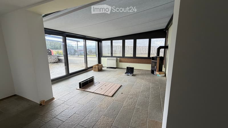 Empty room with large windows, tiled floor, and minimal furnishings including a wooden plank and a small box.