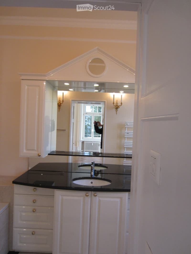 Elegant bathroom with a black countertop, double sink, white cabinets, and a decorative mirror above the sink.