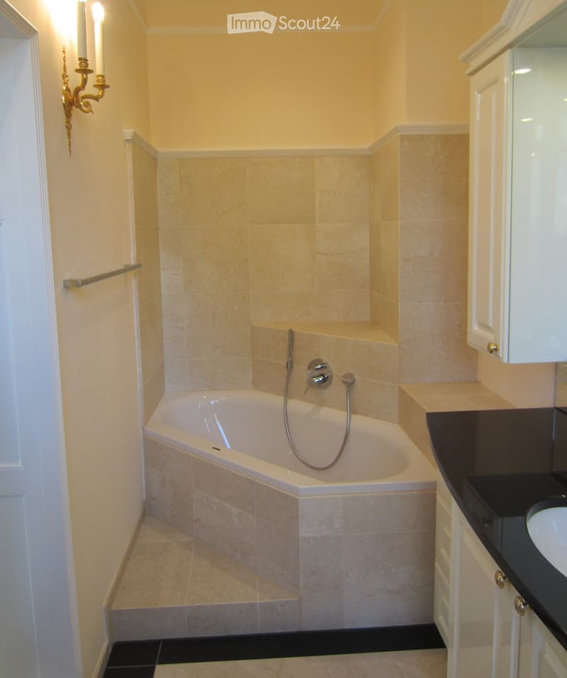 Elegant bathroom with a bathtub, modern faucet, sink, white cabinets, and a decorative wall sconce.