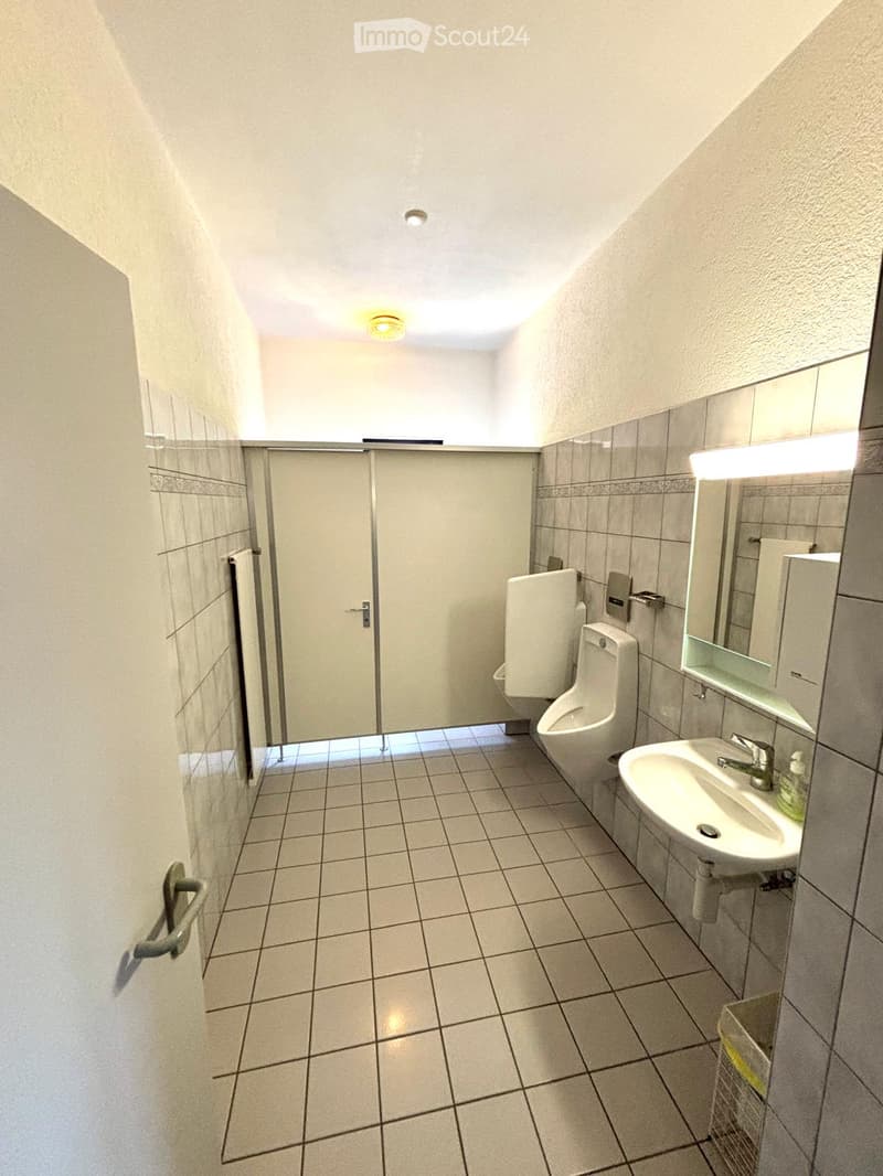 Clean bathroom with tiled walls and floor, featuring a sink, urinal, mirror, and towel. The space is well-lit with recessed lighting.