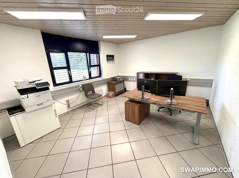 Office space with a wooden desk, two computer monitors, a chair, a printer, and a small cabinet.