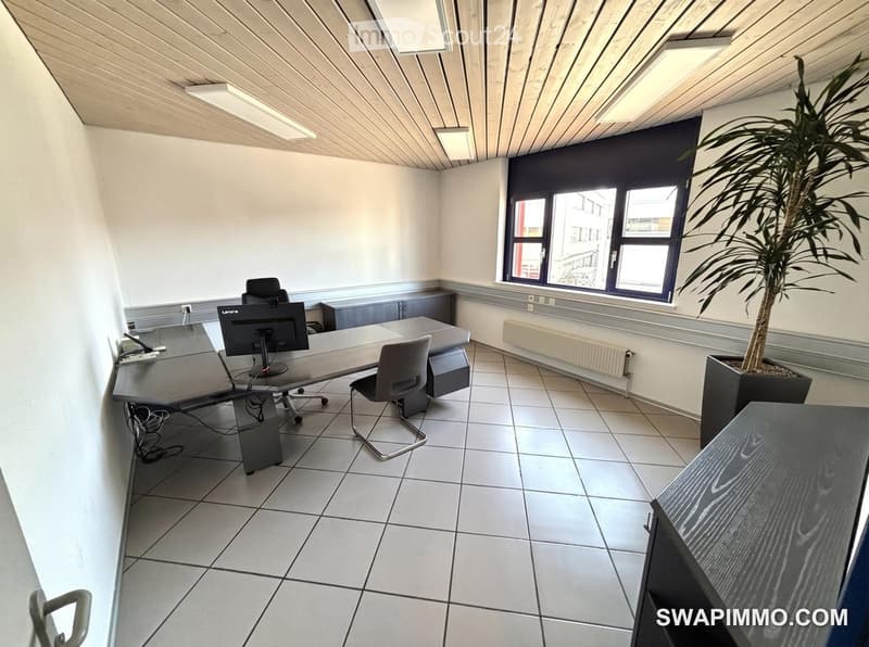 Office space with tiled floor, large window, desk, chairs, computer screen, and potted plant.