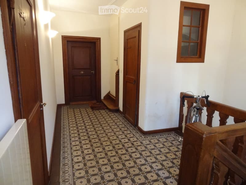 Hallway with patterned tile floor, wooden doors, and a staircase with wooden railing. A bicycle is placed near the staircase.