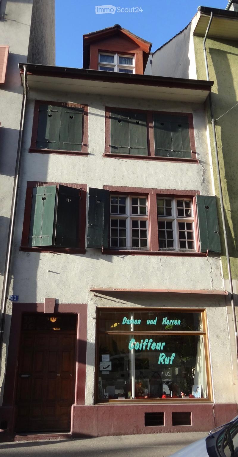 Three-story building with white facade, green shutters, and a storefront labeled 'Goiffeur Ruf' with a window display visible inside.