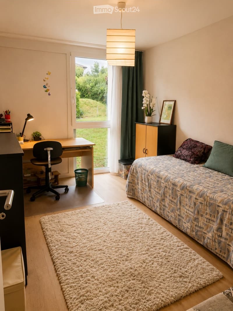 Cozy bedroom with a bed, desk, chair, and a large window offering a view of greenery. Includes a shaggy rug, a lamp, and decorative items.