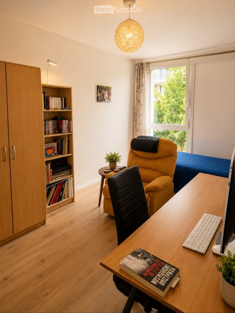 A well-lit bedroom with a wooden floor, a large window with curtains, a desk with a computer, a chair, a sofa, a small table with a plant, a bookshelf, and a picture on the wall.