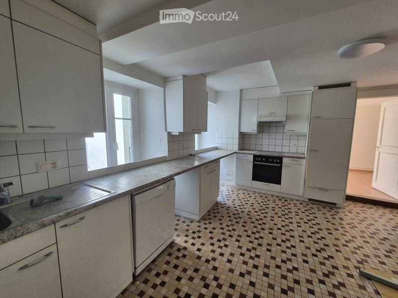 Modern kitchen with white cabinets, granite countertops, and tiled floor. Features a sink, dishwasher, and oven.