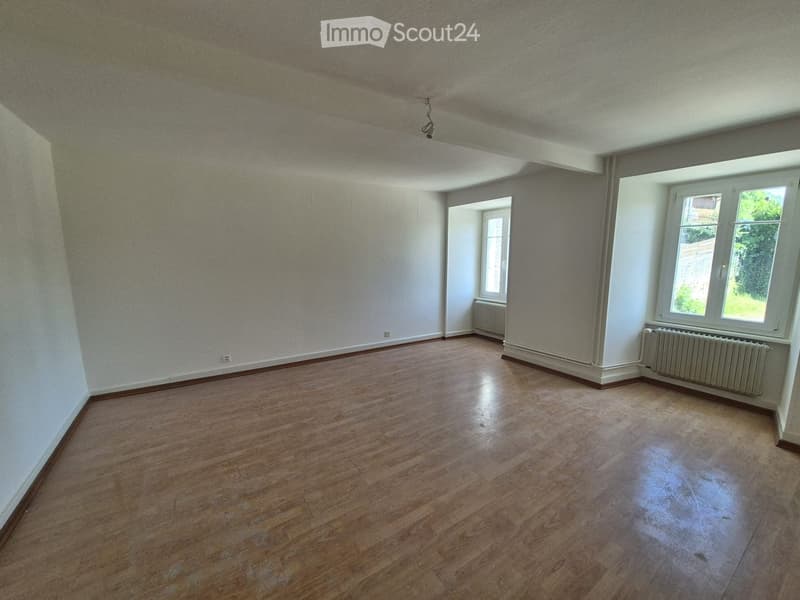 Empty room with wooden flooring, white walls, and two windows with white frames. Radiators are visible beneath the windows.
