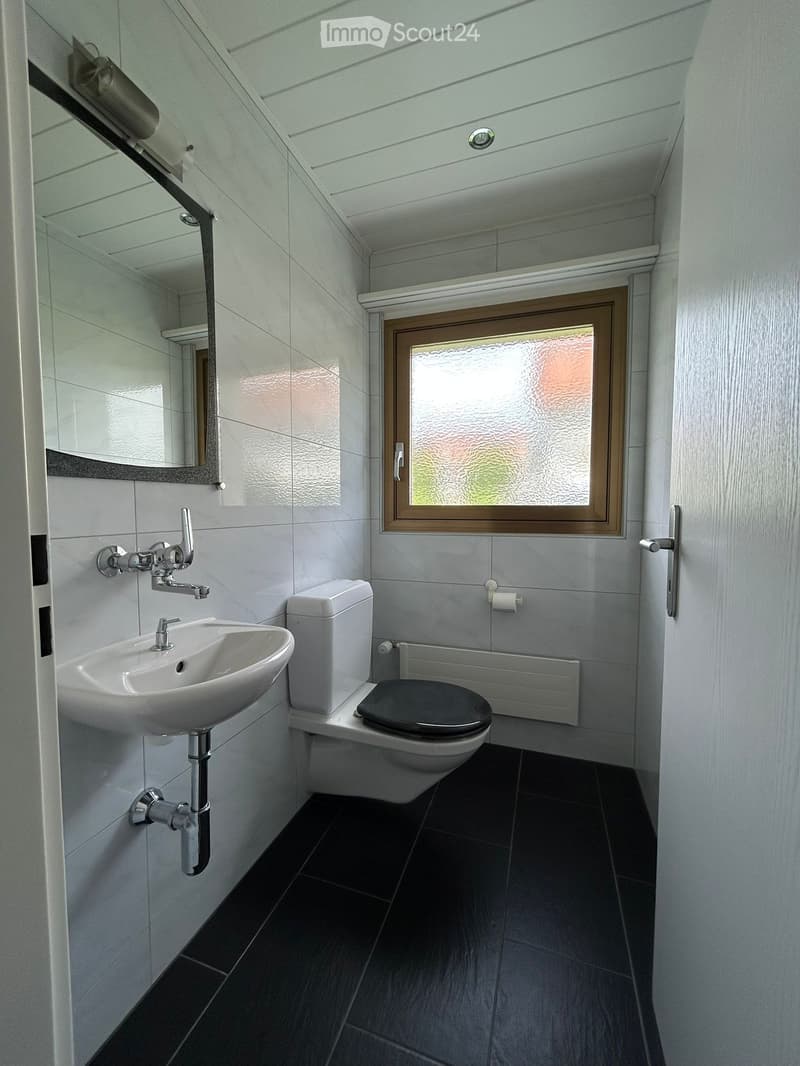 Modern bathroom with white tiles, a black toilet seat, a white sink, and a frosted window. Includes a mirror and a toilet paper holder.