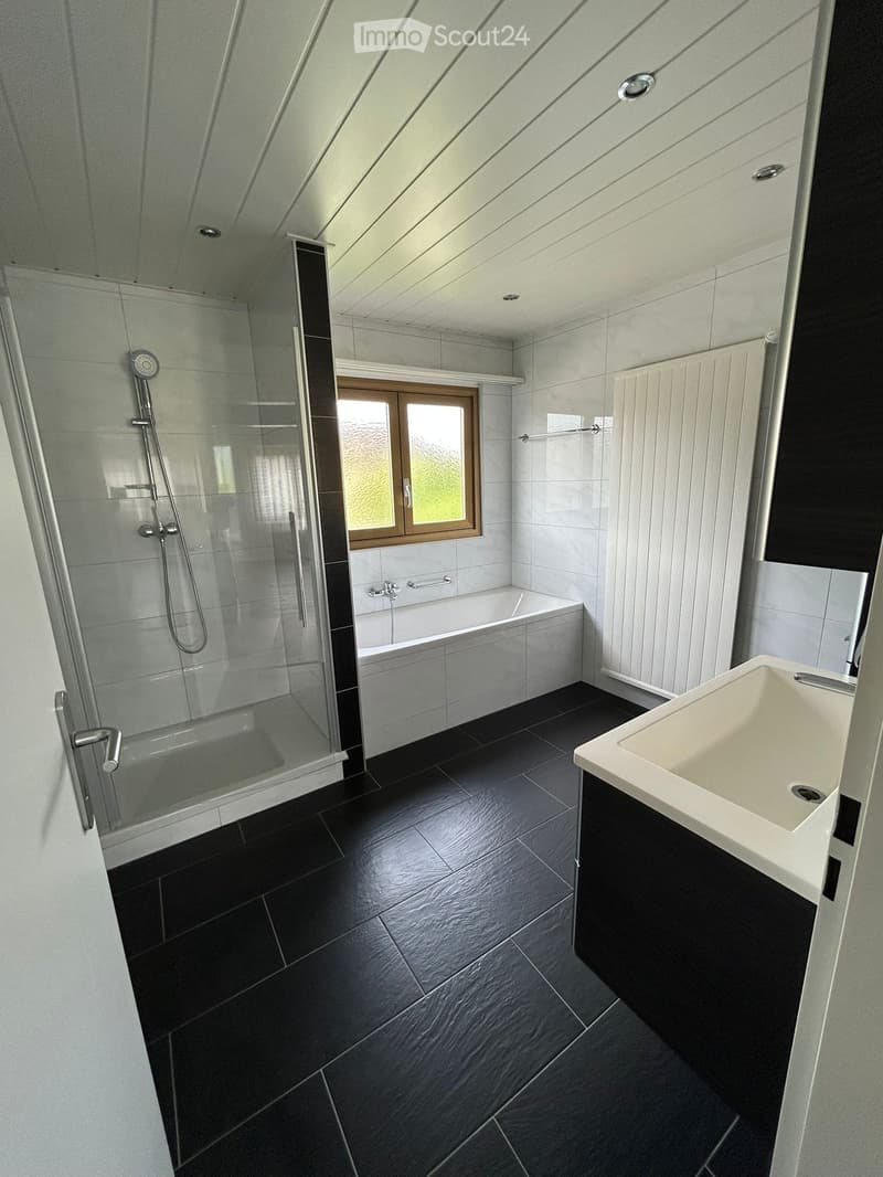 Modern bathroom with a bathtub, sink, shower, and radiator. Features dark tiled flooring and white tiled walls.