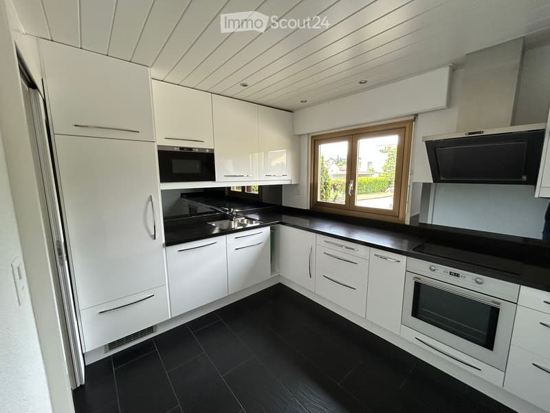 Modern kitchen with white cabinets, black countertops, stainless steel appliances, and a large window offering a view of the outside.