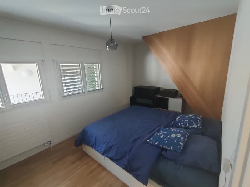 Cozy bedroom with a blue bed, wooden floor, white brick wall, and a slanted ceiling with built-in storage.