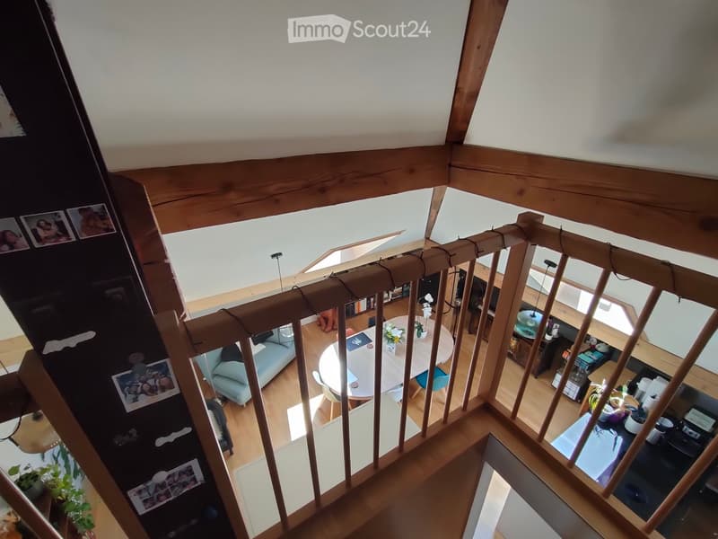 Open-plan living and dining area with a wooden staircase leading to an upper level, featuring a light blue sofa, a round dining table with chairs, and a kitchen area with various appliances and counter space.